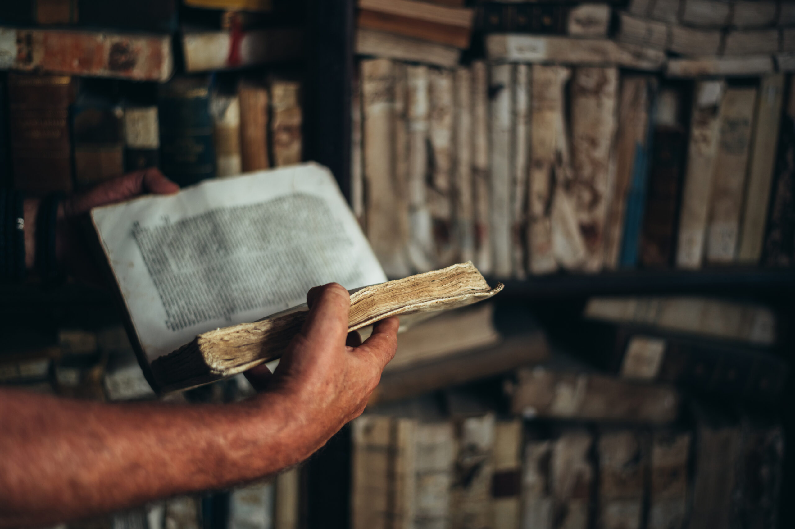 Hands holding open an old book in a library, showcasing print preservation efforts.