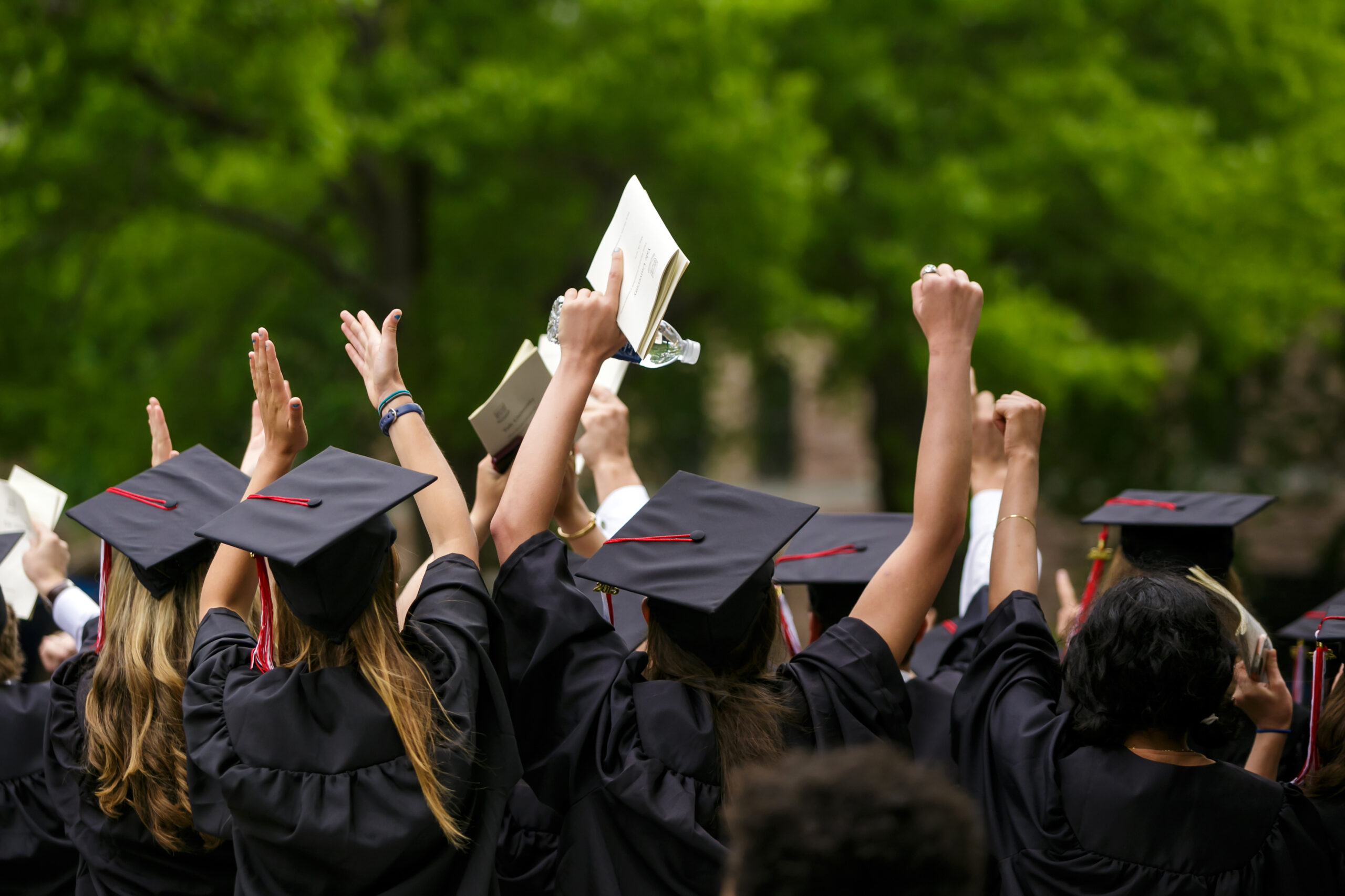 Graduates in gowns celebrate graduation day with raised hands and books.